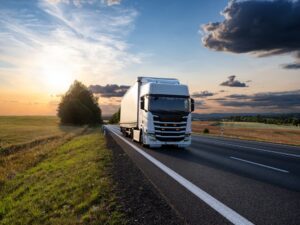 White truck driving on the asphalt road in rural landscape at sunset