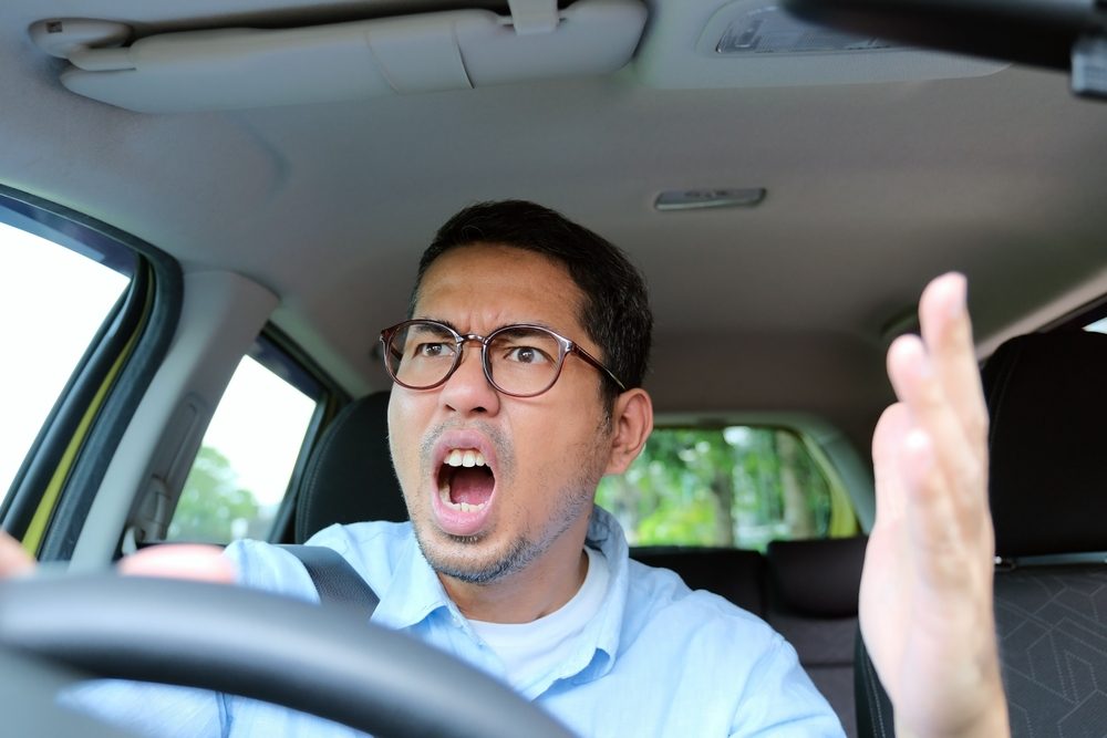 An angry man driving a car. What is the difference between aggressive driving and road rage?