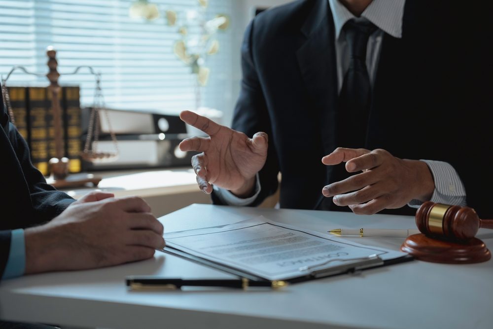 Closeup view of a lawyer from the neck down sitting at a desk and discussing a personal injury structured settlement with a client.